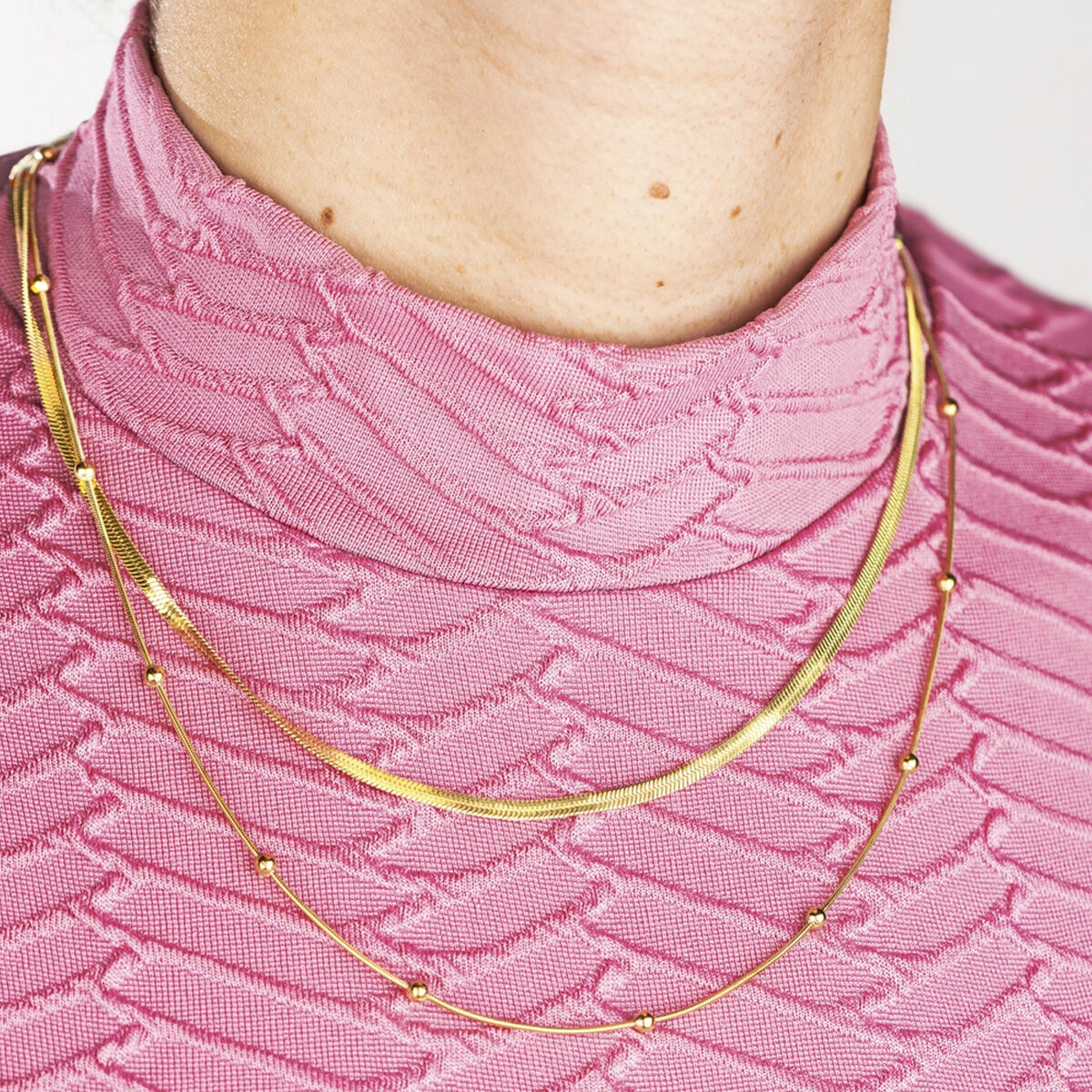 Detail van de gouden Lotus ketting met elegante afwerking, gedragen op een roze top.