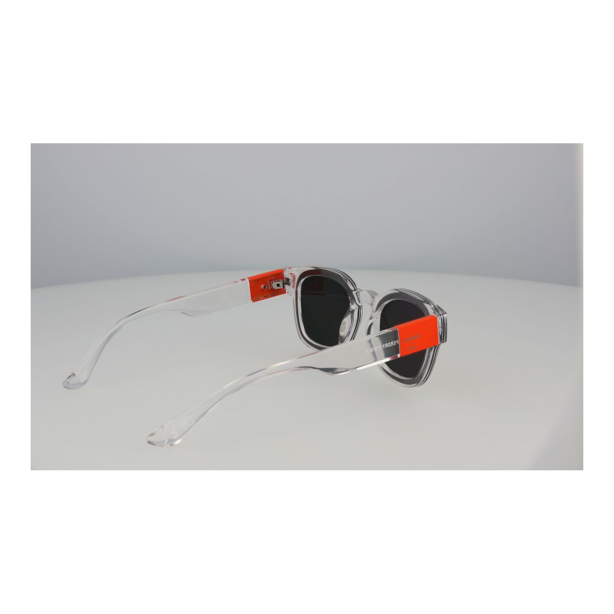 Zijaanzicht van de Superdry SDS XMONO zonnebril met transparante montuur en oranje details.