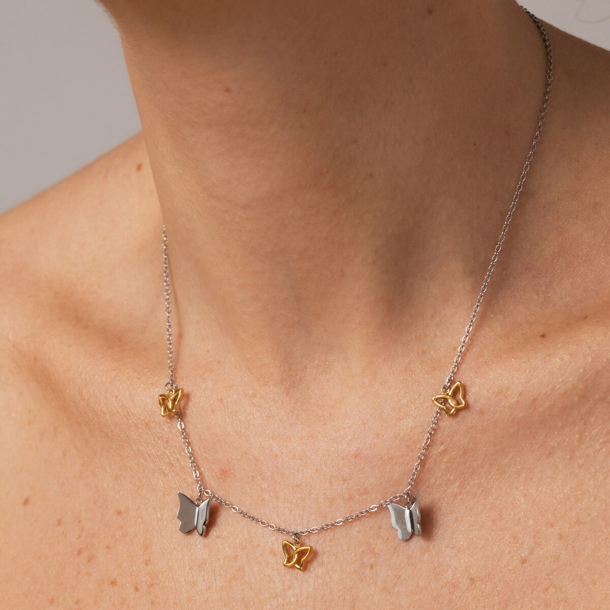 Zilverkleurige One Jewels ketting met gouden vlinderdetails, elegant gedragen om de hals.