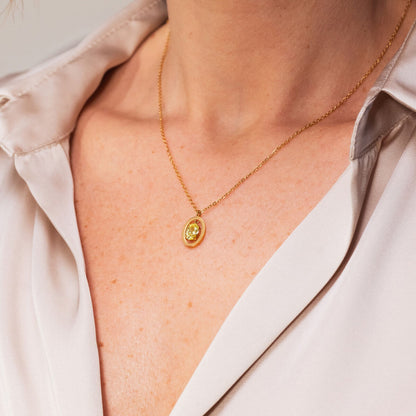 Close-up van de gouden One Jewels ketting met een elegante hanger, gedragen op een lichte blouse.