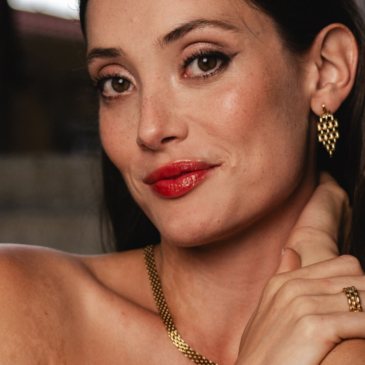 Elegante gouden One Jewels oorbellen, gedragen door een vrouw met een stralende glimlach.
