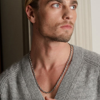 Zilverkleurige One Jewels ketting gedragen door man in casual grijze trui.