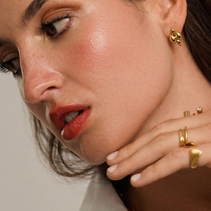 Close-up van een vrouw die de gouden One Jewels oorbellen elegant draagt.