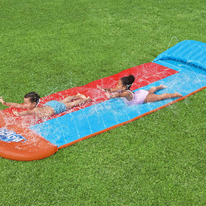 Kinderen glijden samen van de Bestway H2OGO Tsunami Splash Ramp op een groene grasmat.