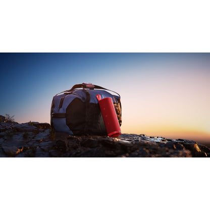 Rode Xiaomi Bluetooth luidspreker leunend tegen een zwarte tas bij zonsondergang.