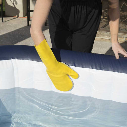 Detail van een hand met een gele schoonmaakhandschoen die de rand van de Lay-Z-Spa aanraakt.