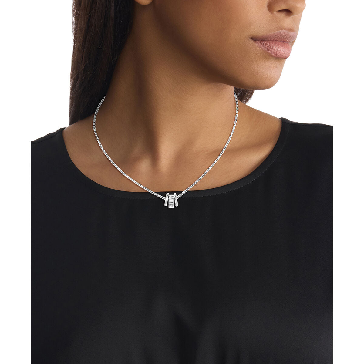 Detail van de Calvin Klein ketting in roestvrij staal, gedragen door een vrouw in een zwarte top.