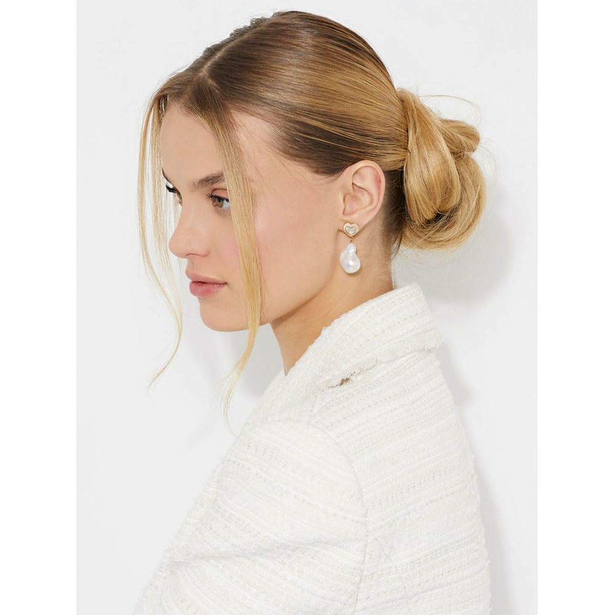 Detail van de Guess oorbellen met een elegante parel en hartvormig ontwerp, gedragen door een model.