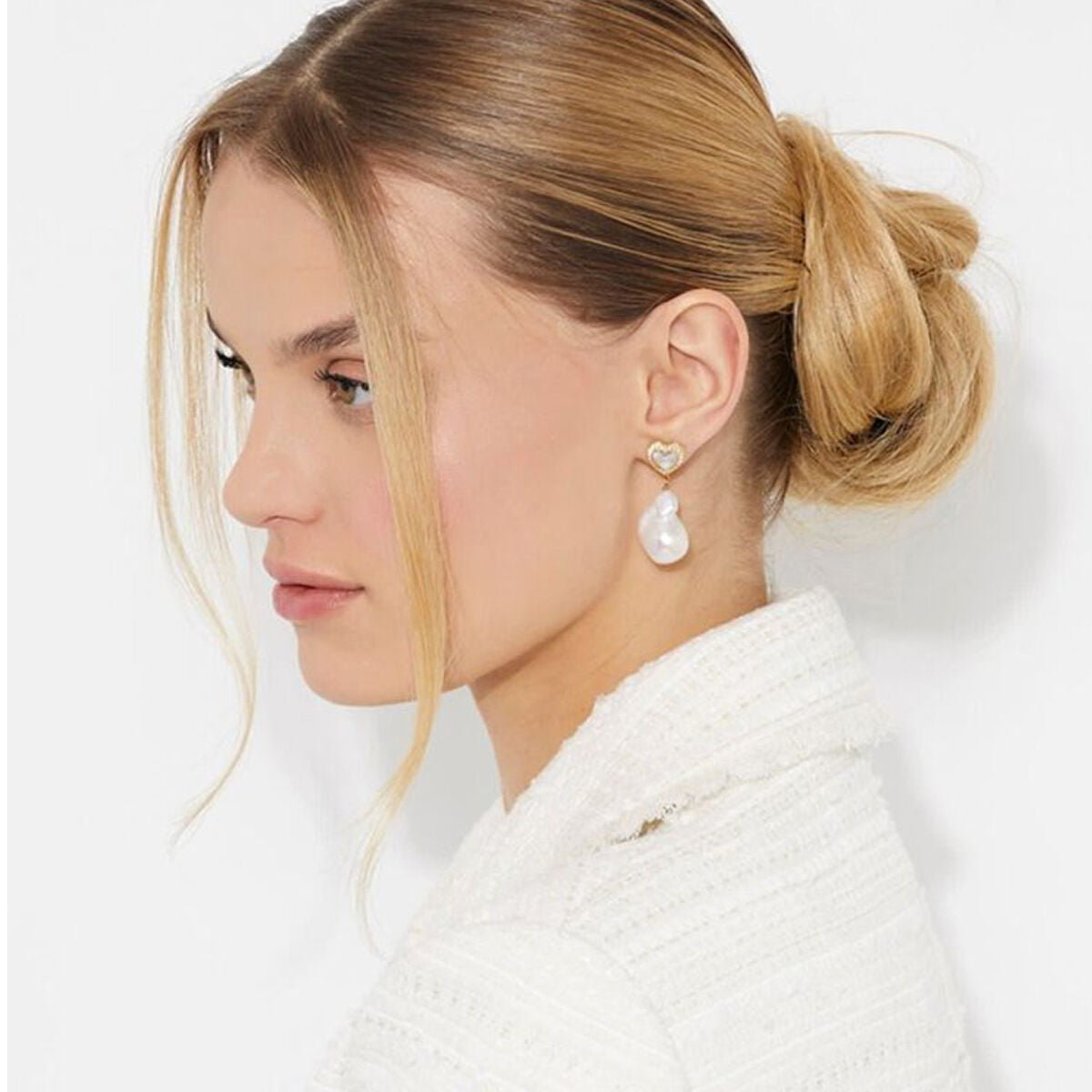 Zijaanzicht van een vrouw met Guess oorbellen, featuring een elegante parel en hartvormige detail.