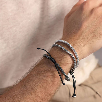Zilverkleurige Albert M. armband gedragen met andere armbanden op een pols.
