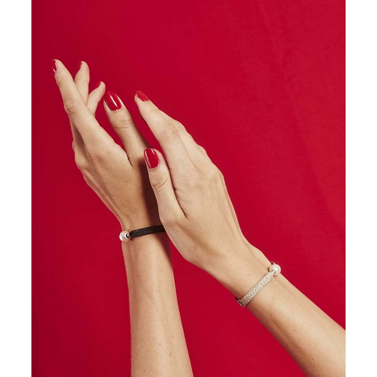Zwarte Majorica armband elegant om een pols met rode nagellak, tegen een rode achtergrond.
