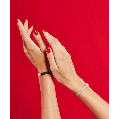 Zwarte Majorica armband elegant om een pols met rode nagellak, tegen een rode achtergrond.