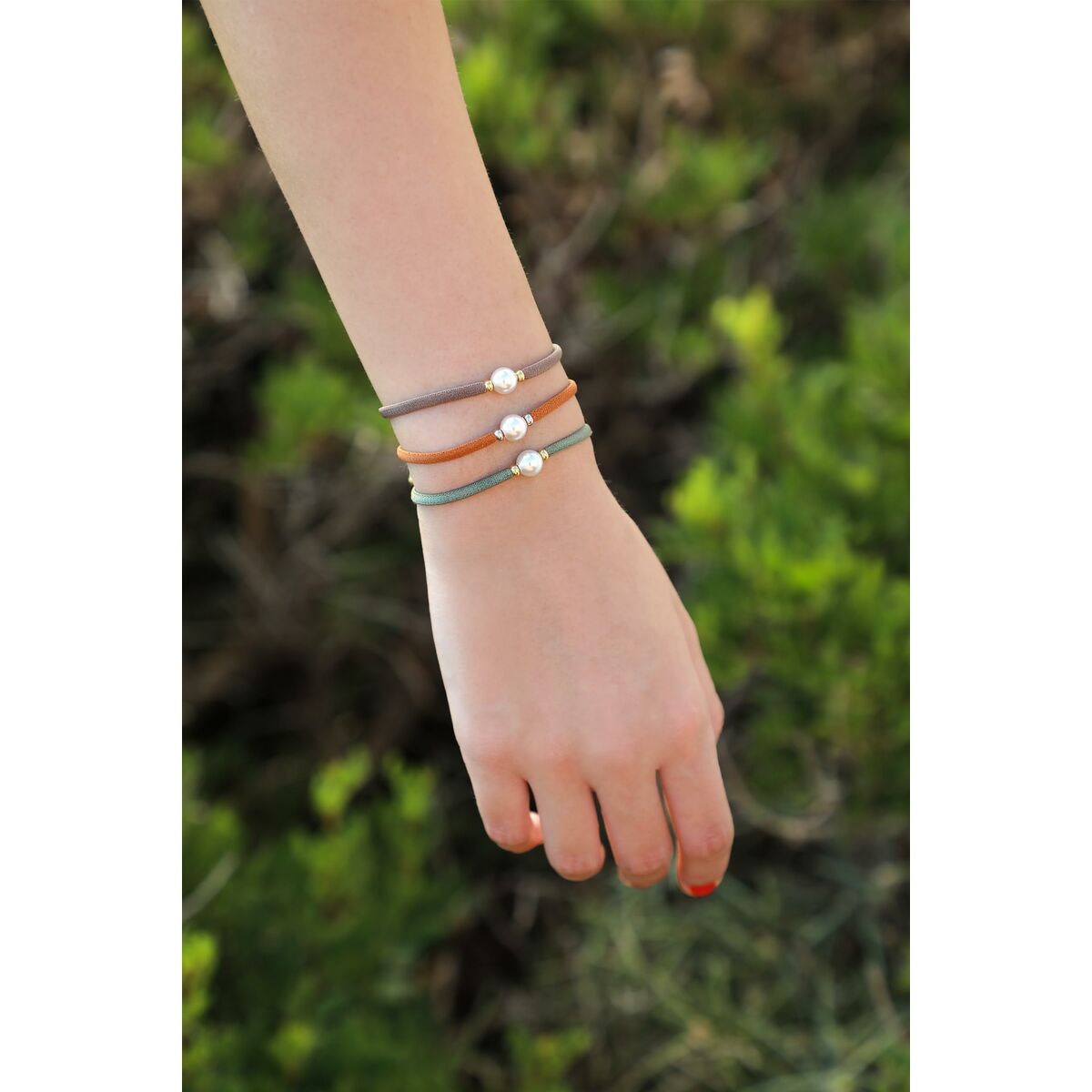 Detail van de Majorica armband met parels, gedragen om een hand in een groene omgeving.