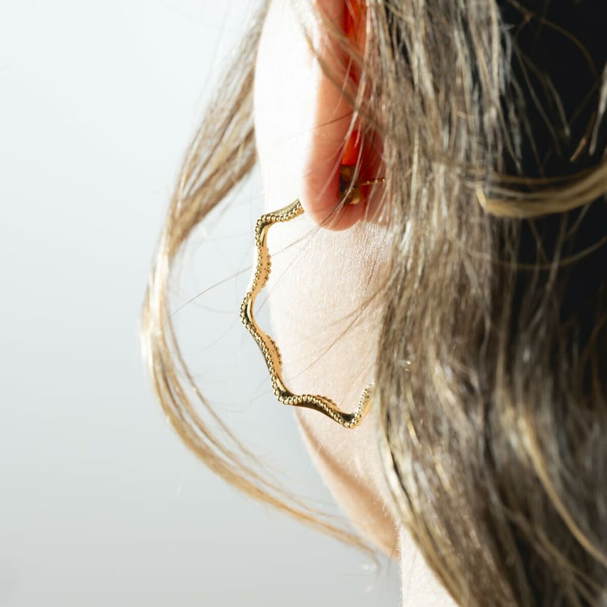 Detail van de gouden Lotus oorbellen met elegant design, gedragen aan een oor.