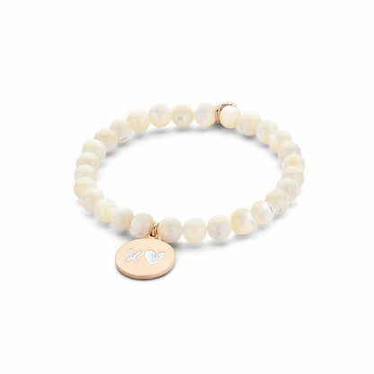 Detail van de witte CO88 Collection armband met gouden hanger en parelmoerachtige kralen.