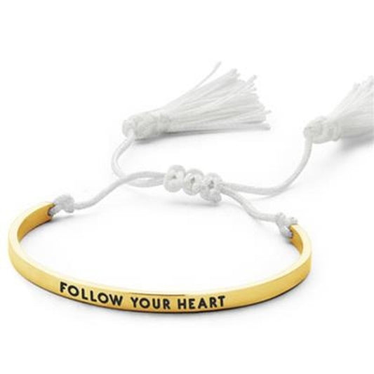 Gouden CO88 Collection armband met de tekst "FOLLOW YOUR HEART" en witte kwastjes.