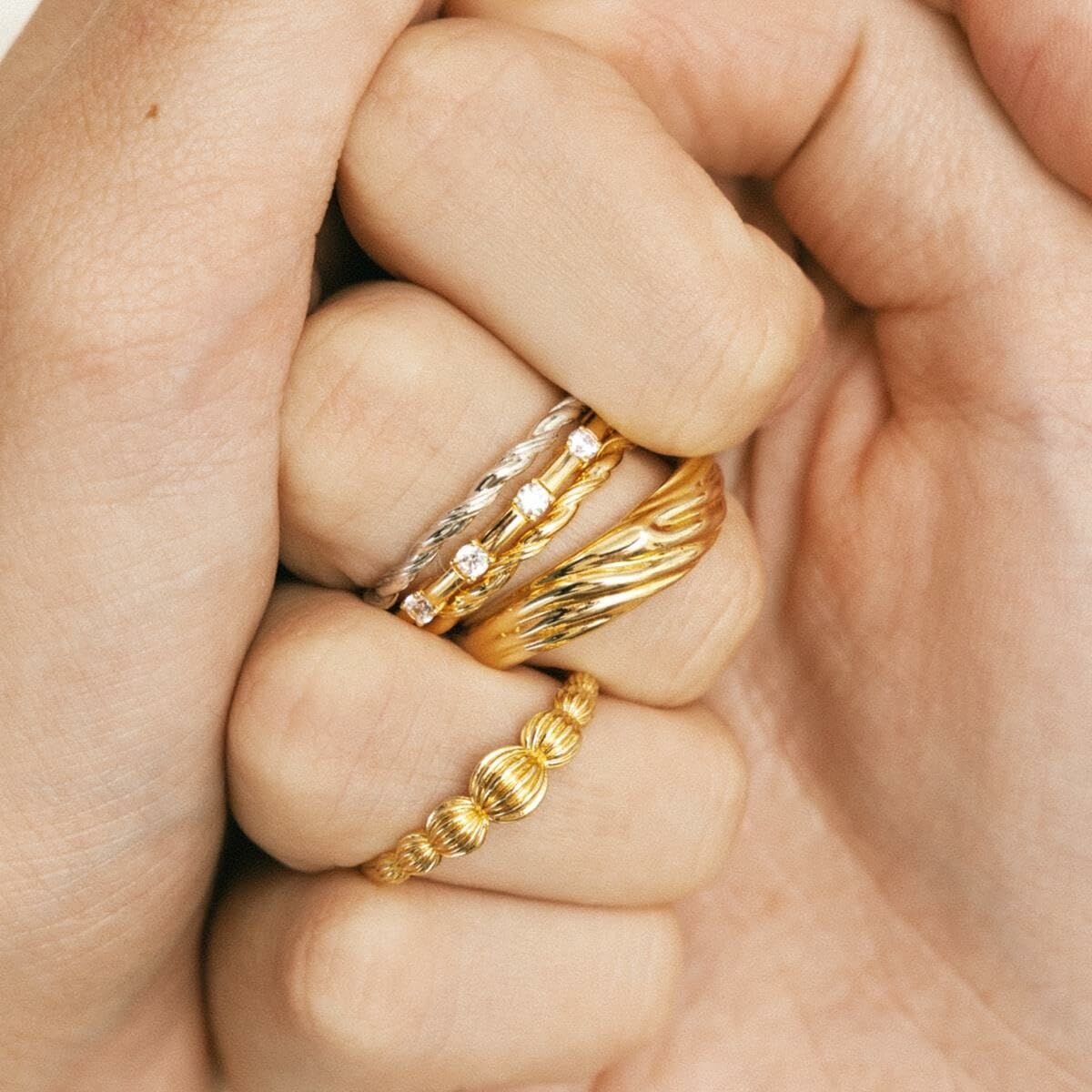 Detail van de 24KAE ring met elegante gouden afwerking, gedragen op meerdere vingers.